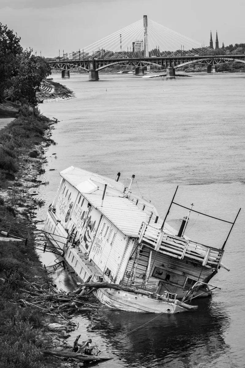 Sunken boat tilted on a riverbank beneath distant bridges